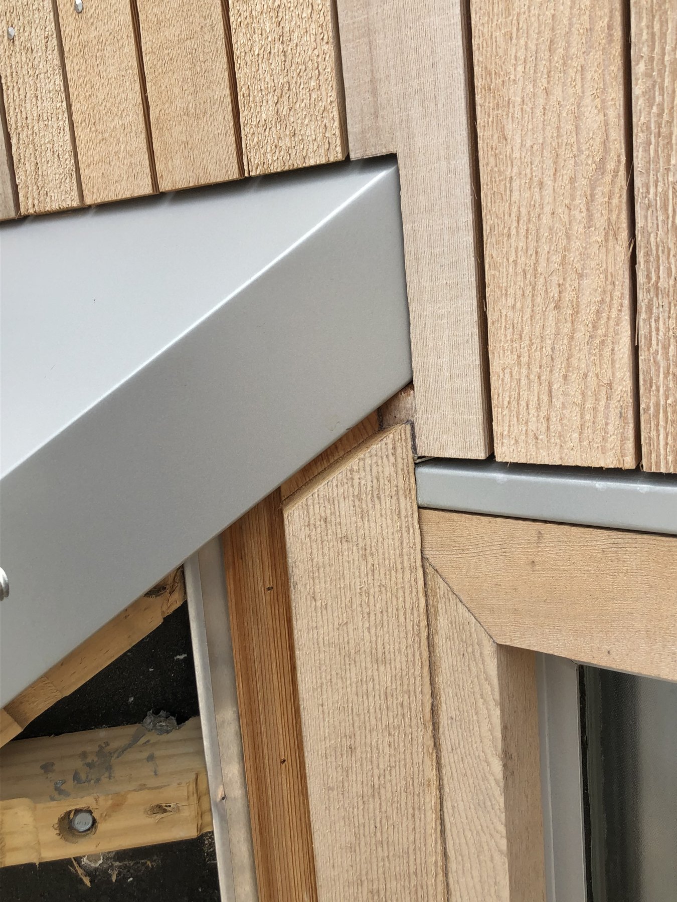 Close-up of cedar cladding meeting a metal flashing and window junction