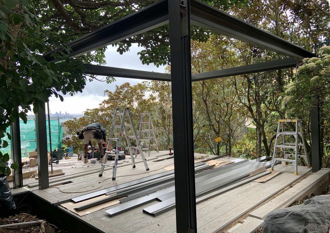 Louvred pergola framework installation in progress among trees in Mission Bay