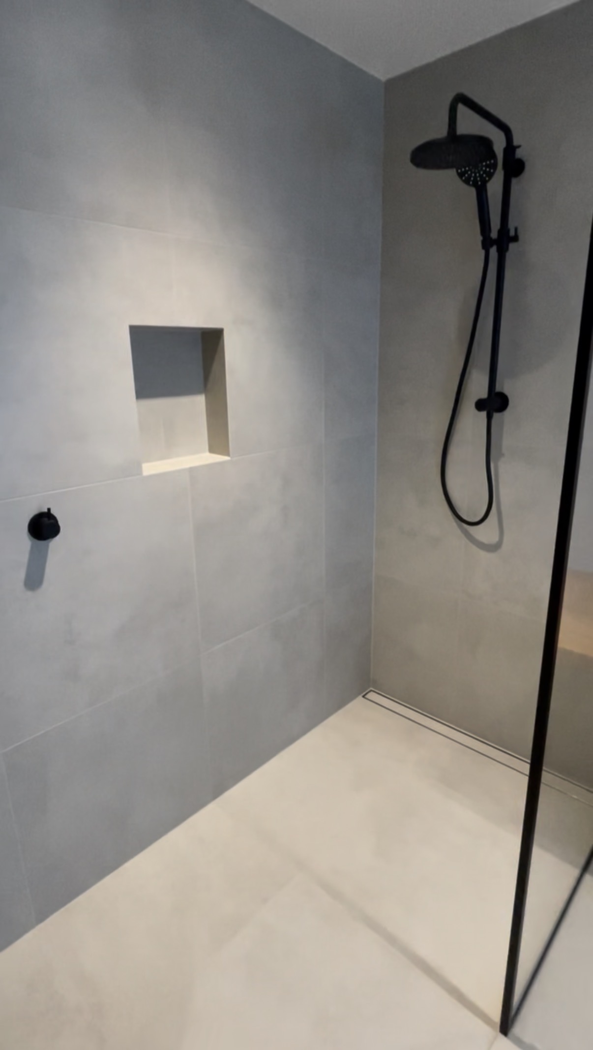 The completed tiled shower, with a recessed niche and black fittings.